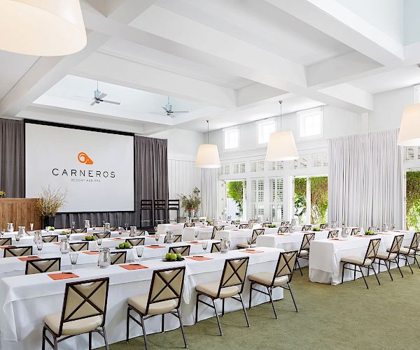 A bright, spacious conference room set up for a meeting with tables, chairs, and a large screen displaying