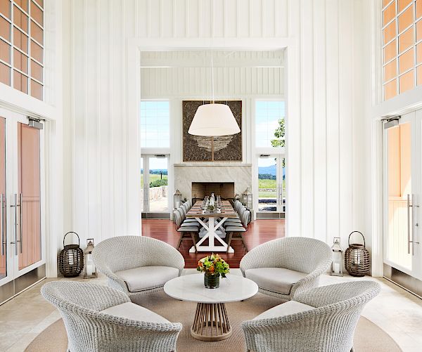 A bright room with wicker chairs around a table, lanterns by the doors, and a modern fireplace in the background.