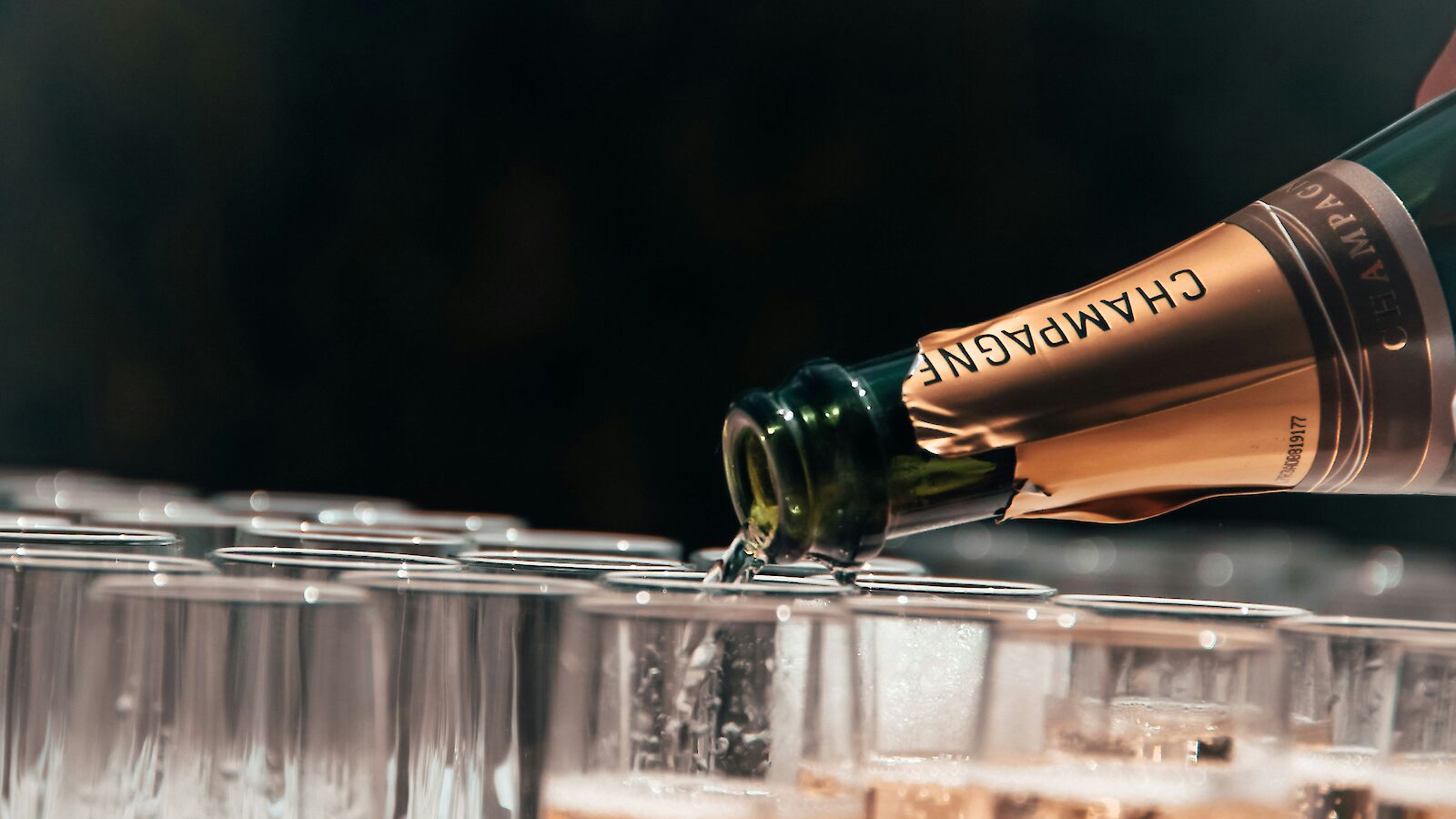 A bottle of champagne is being poured into a row of clear glasses, creating a festive and celebratory atmosphere.