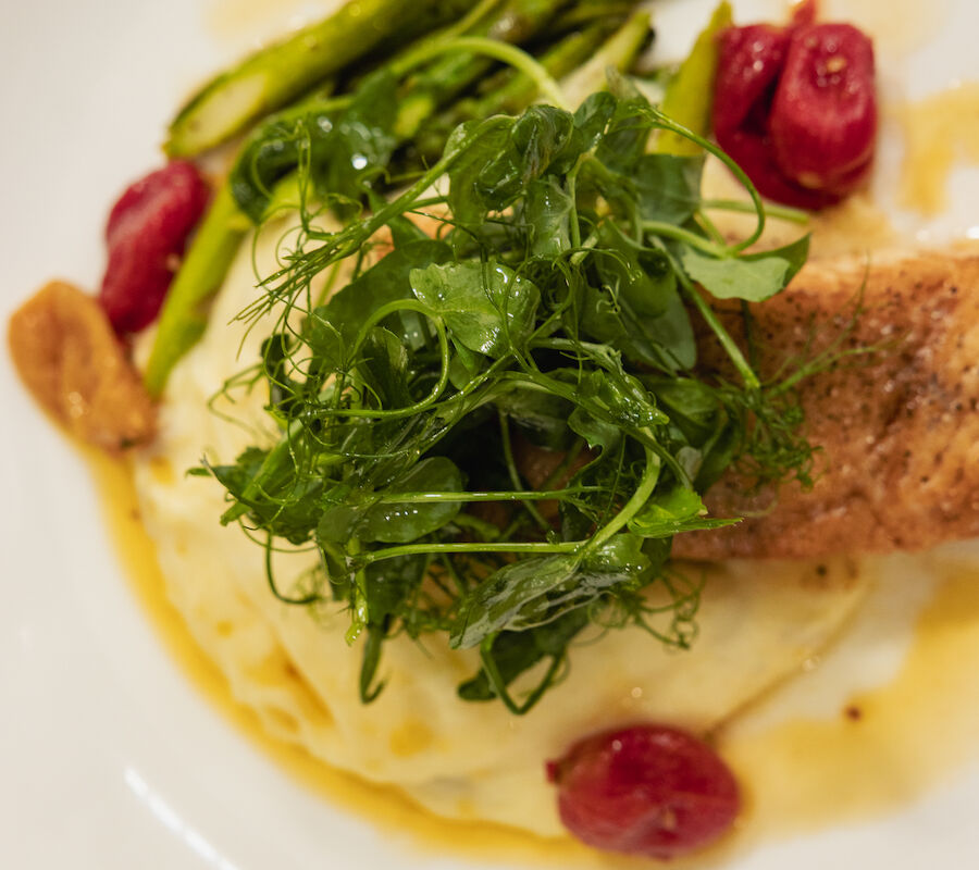 The image shows a dish with mashed potatoes, asparagus, cherry tomatoes, microgreens, and a portion of meat in a sauce.