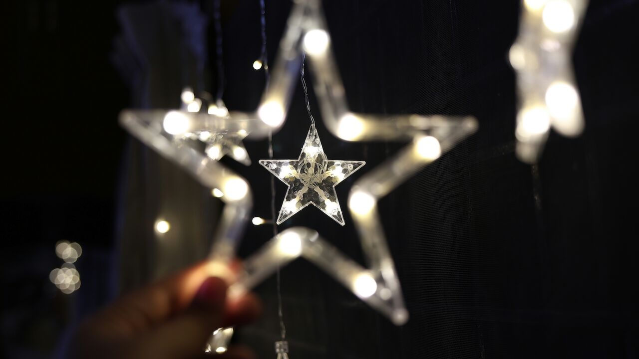 The image shows illuminated star-shaped decorations, some held by a hand, set against a dark background.