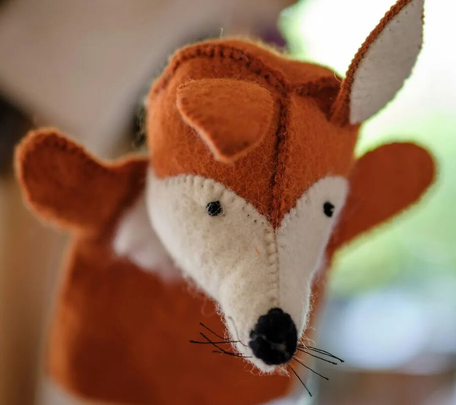 The image shows a handcrafted felt fox puppet with orange and white fabric, featuring a pointed nose and stitched details.