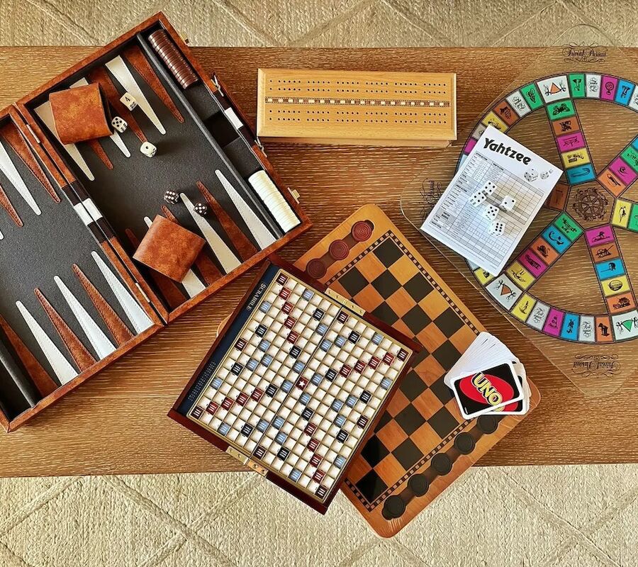 The image shows various board games: backgammon, Scrabble, a cribbage board, Yahtzee, Uno cards, and a Trivial Pursuit board.