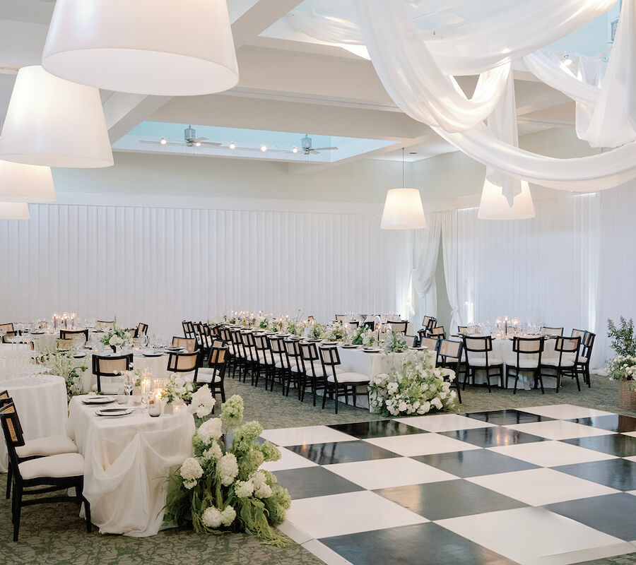 The image shows an elegant wedding reception setup with draped fabric, floral arrangements, dining tables, and a checkered dance floor.