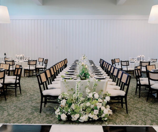 The image shows a beautifully set dining table for an event, with elegant chairs, floral centerpieces, and soft lighting.