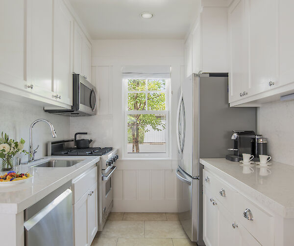 A modern kitchen with white cabinets, stainless steel appliances, flowers, and a view of trees through the window completes the space.