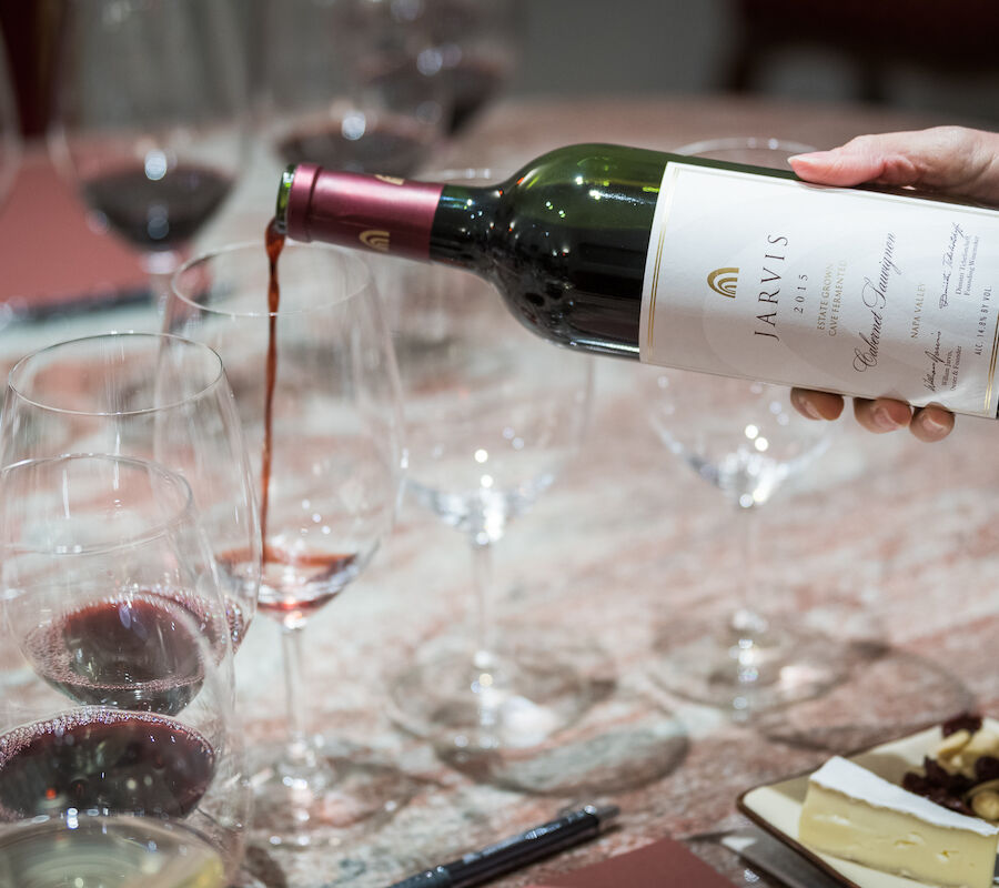 A hand is pouring red wine from a bottle labeled 