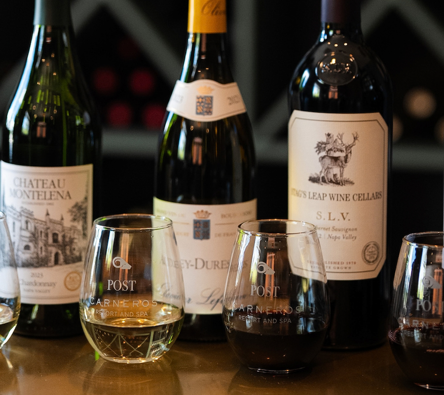 The image shows five bottles of wine and three glasses on a table, each labeled with 