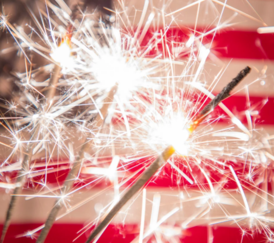 Sparklers are lit against the backdrop of an American flag, creating a festive and patriotic scene.