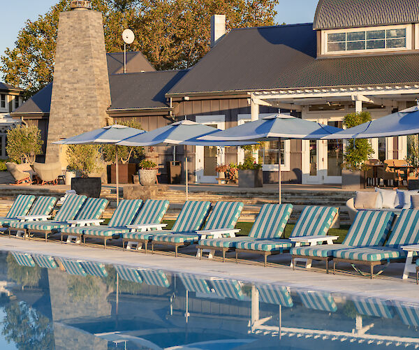 The image shows a poolside area with striped lounge chairs and umbrellas in front of a large building, possibly a resort or hotel.