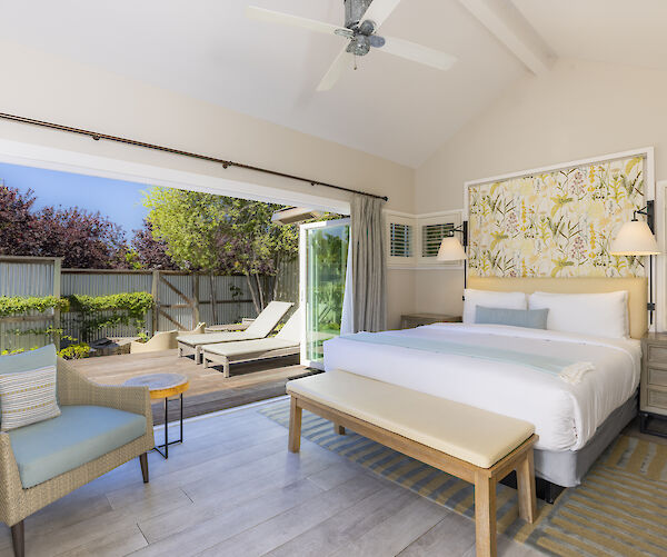 A bright, modern bedroom with an open patio door leading to an outdoor deck with sun loungers and greenery.