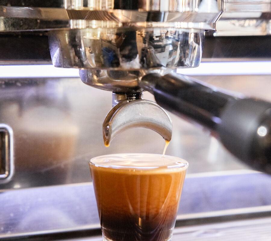 The image shows an espresso machine pouring coffee into a glass on the drip tray.