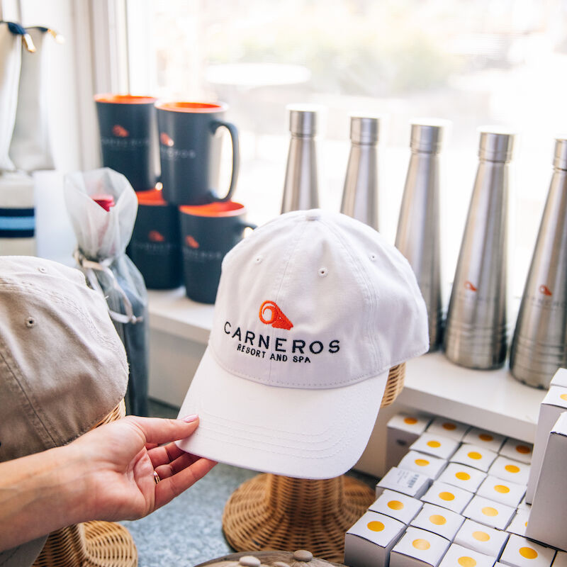 A display of branded merchandise, including hats, bottles, mugs, and boxes, with a hand holding a cap.