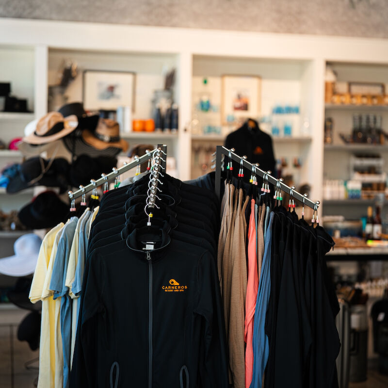 A clothing rack with various shirts is in a store, surrounded by shelves with hats and other items on display.