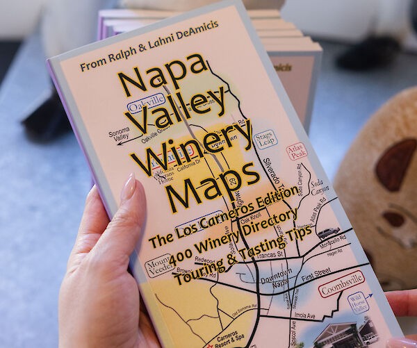 A person holds a Napa Valley Winery Maps guide, detailing 400 wineries and tips. The cover shows a partial map and a vintage truck illustration.