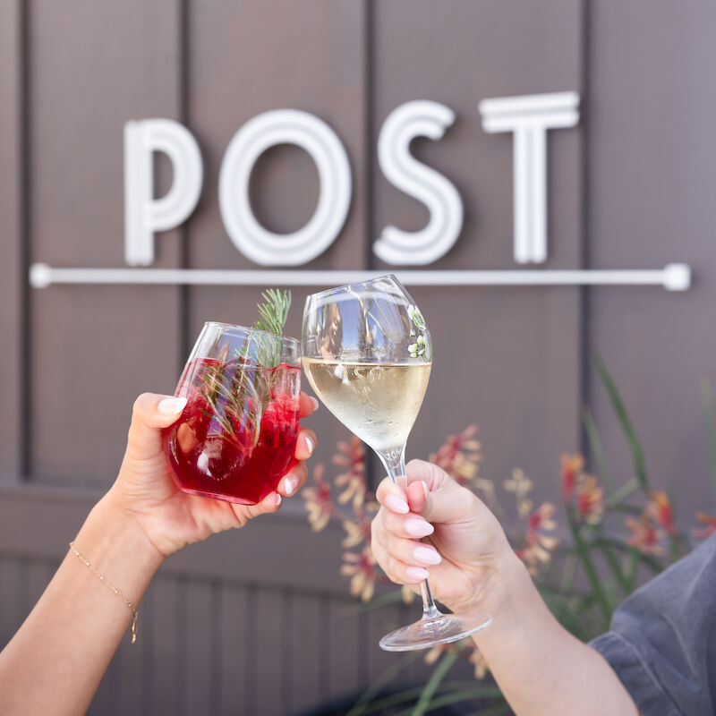 Two people clink wine glasses—one with red sangria, the other with white wine. A sign in the background reads 