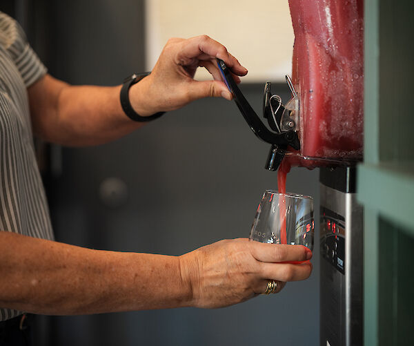 A person is dispensing a red beverage into a glass from a machine.