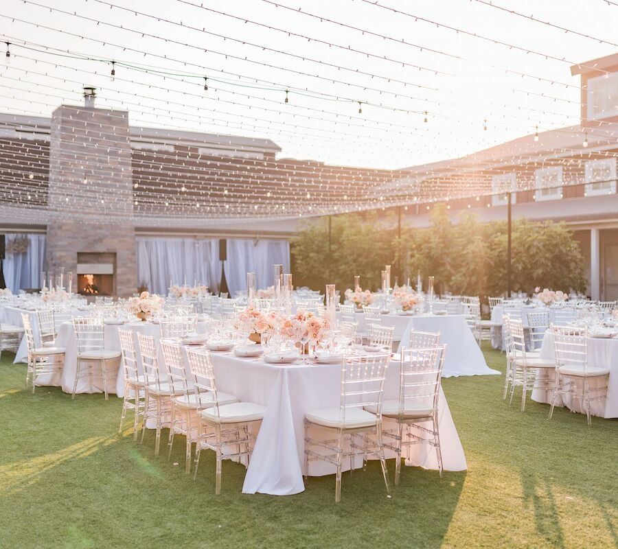 An elegant outdoor wedding reception setup with decorated tables and chairs under string lights during sunset.
