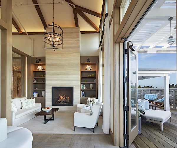 A modern living room with a fireplace, cozy seating, and open shelves, connected to an outdoor patio area with lounge chairs and a stunning view.