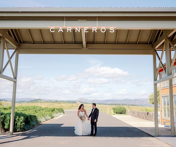 A couple in wedding attire stands under a structure with 
