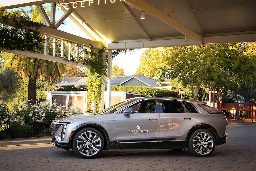 A sleek silver SUV is parked under a canopy adorned with greenery, next to a building amidst lush surroundings.