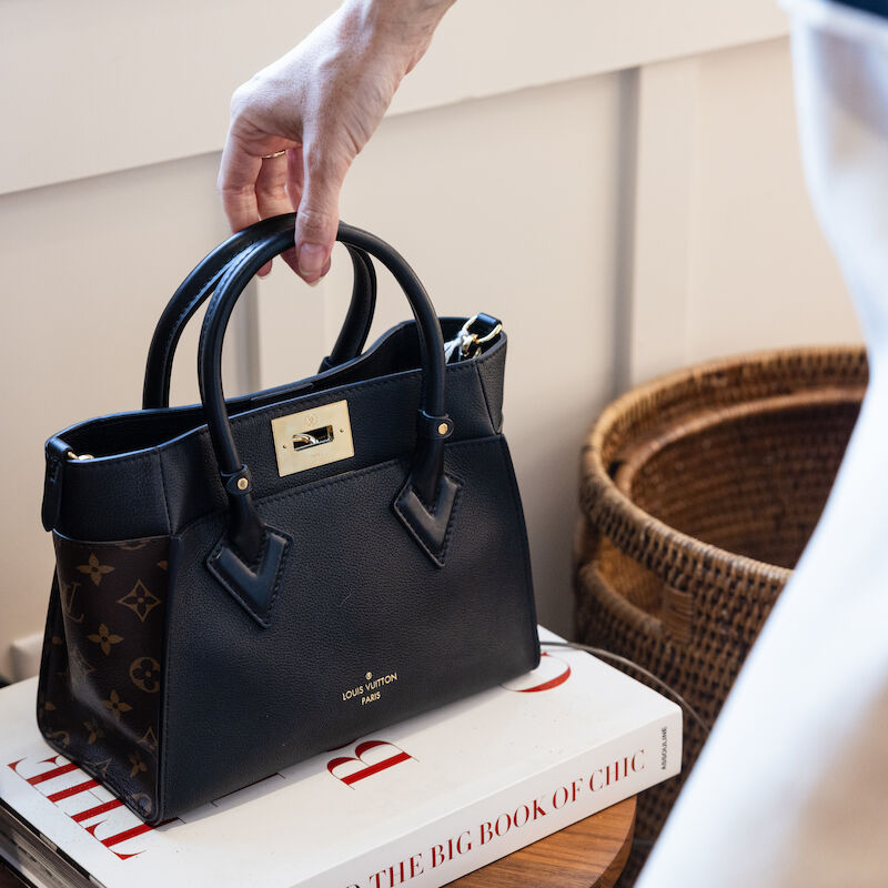 A person is picking up a stylish handbag resting on a book titled 