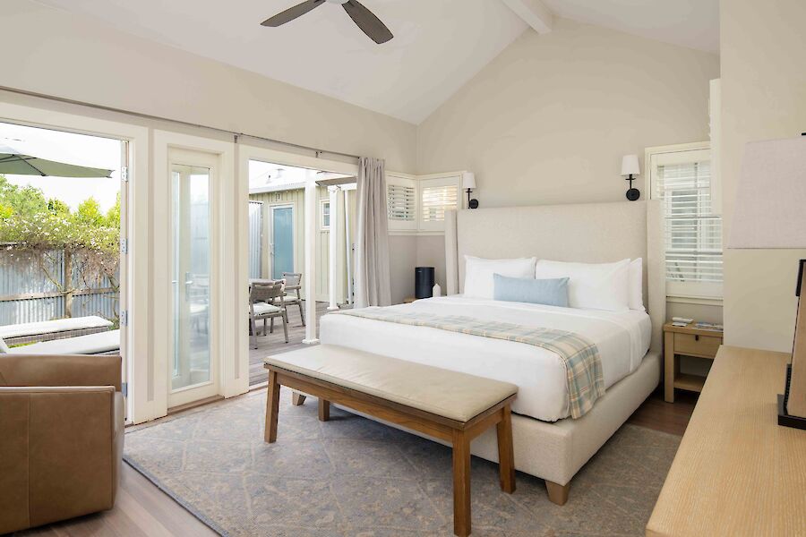 A cozy bedroom with a large bed, bench, nightstands, and an outdoor patio view through glass doors completes the scene.