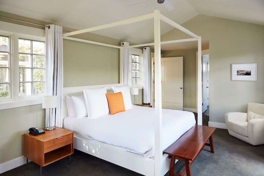 A neatly arranged bedroom featuring a four-poster bed, side tables, a bench, and an armchair, all in a softly lit, cozy setting.