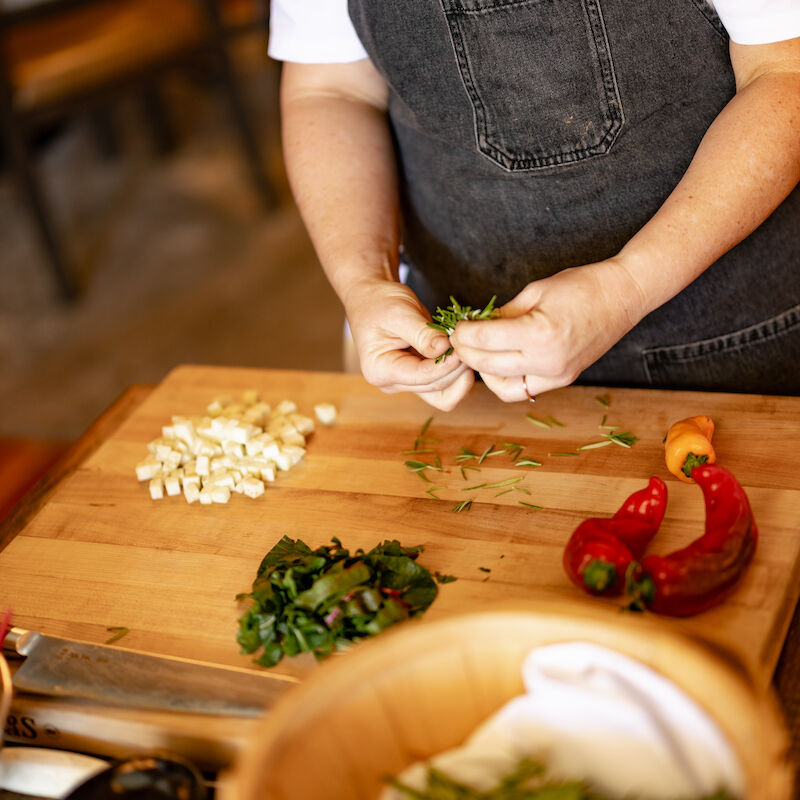 A person wearing an apron is preparing vegetables on a wooden cutting board with chopped garlic and peppers nearby.