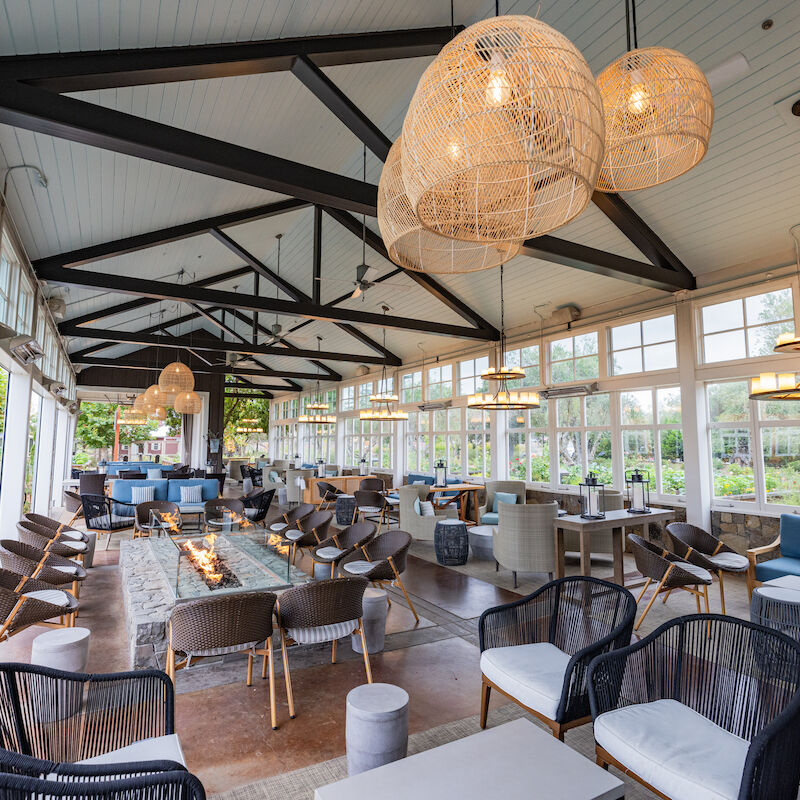 The image shows a spacious, modern restaurant with large windows, stylish seating, and decorative light fixtures.