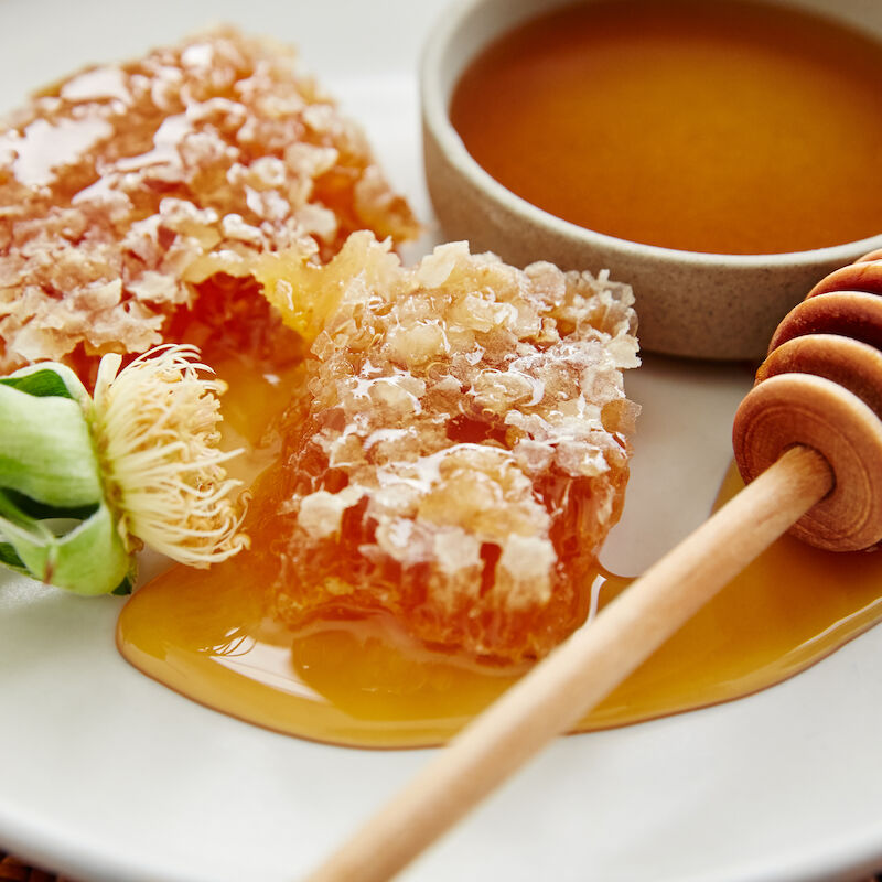 The image shows honeycomb pieces, a honey dipper, a bowl of honey, and a flower on a plate.