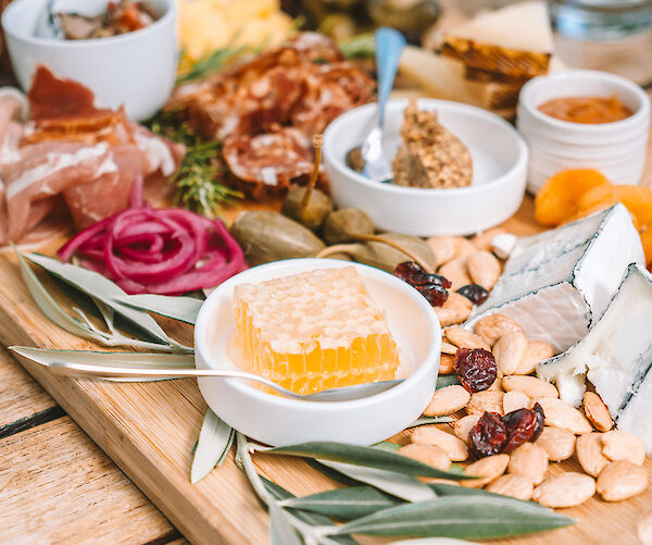 A charcuterie board with meats, cheeses, nuts, honeycomb, mustard, and pickles on a wooden table.