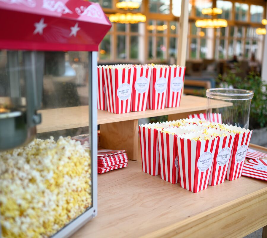 A popcorn machine and striped popcorn boxes on a wooden table, with a cozy, well-lit setting in the background.