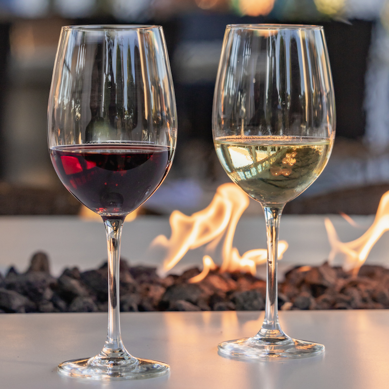 Two wine glasses, one with red wine and the other with white wine, are set on a table near a decorative fire pit.