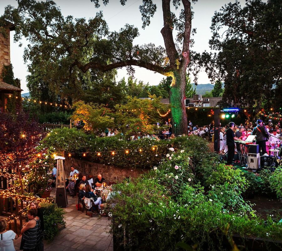 Outdoor party with string lights and people gathered in a garden setting. An Italian flag is displayed on the building.