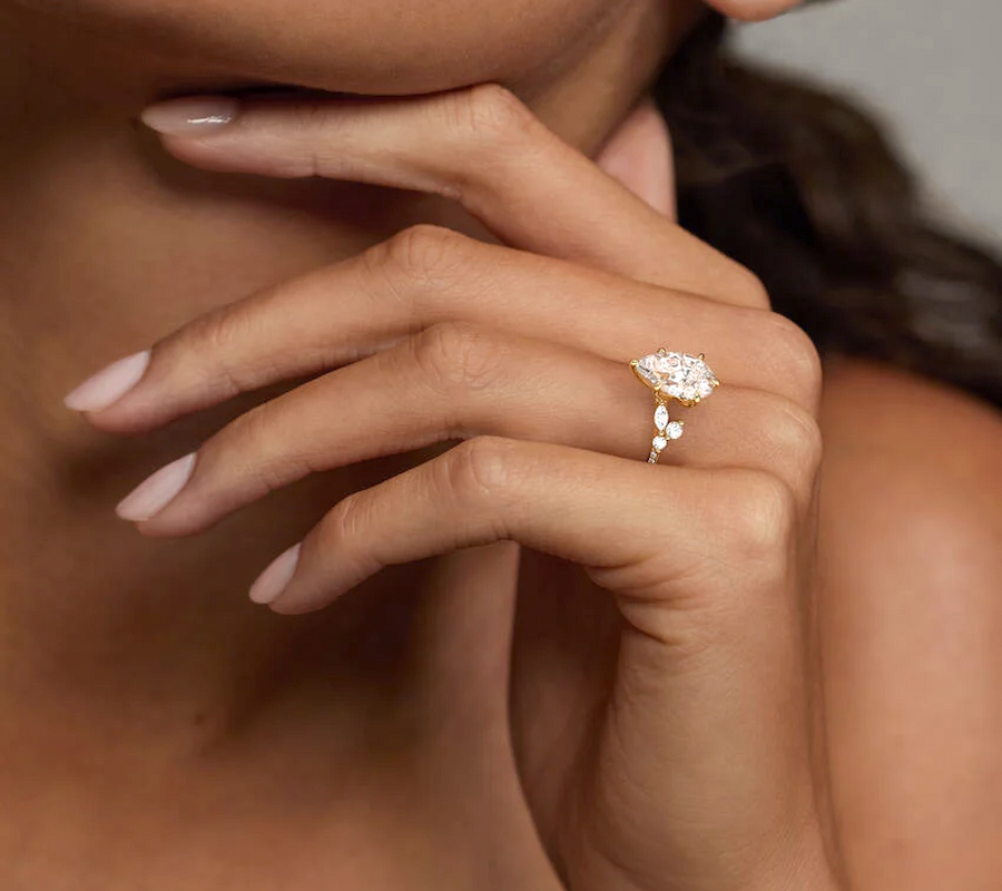A close-up of a woman’s hand wearing a ring with a large, eye-catching gemstone, elegantly posed near her face.