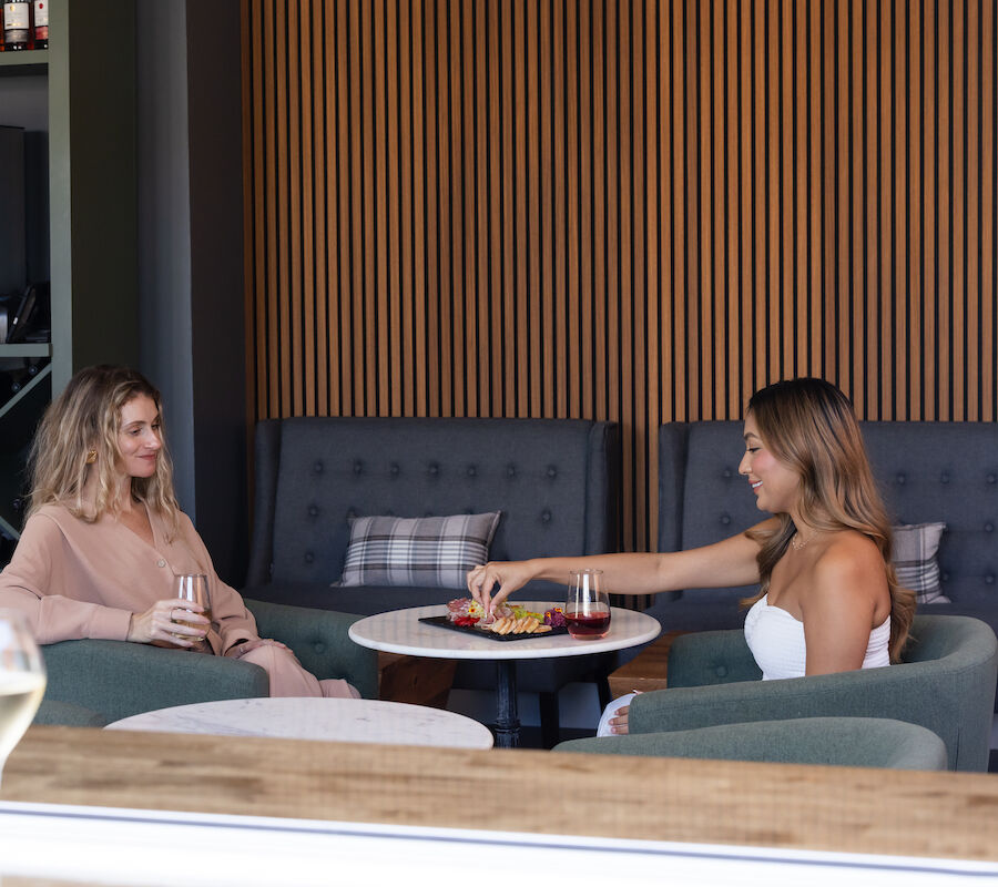 Two people are seated at a table in a lounge, enjoying drinks and snacks.